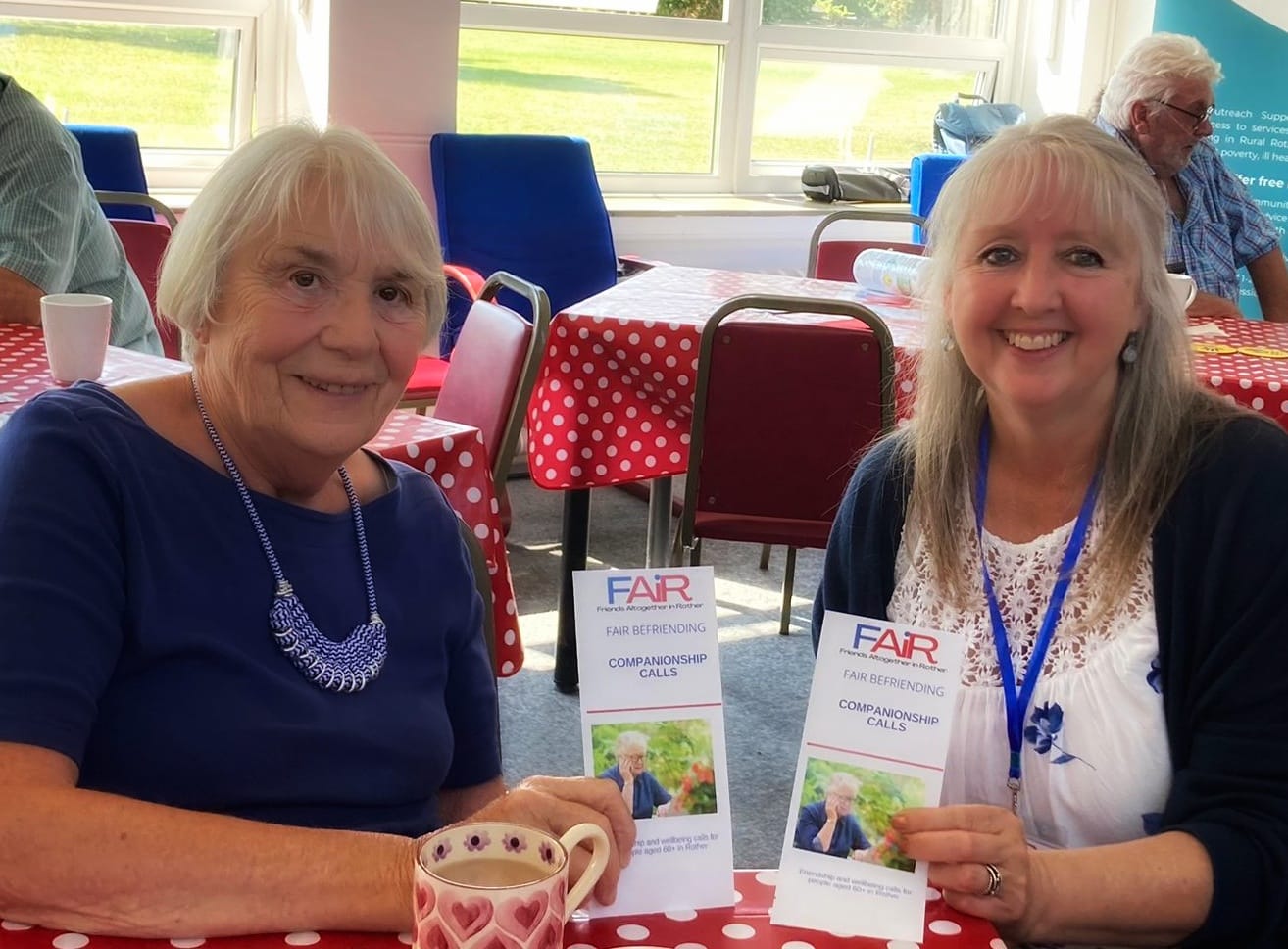 Image shows Befriending Coordinator and visitor to event holding leaflets about the FAiR telephone befriending service